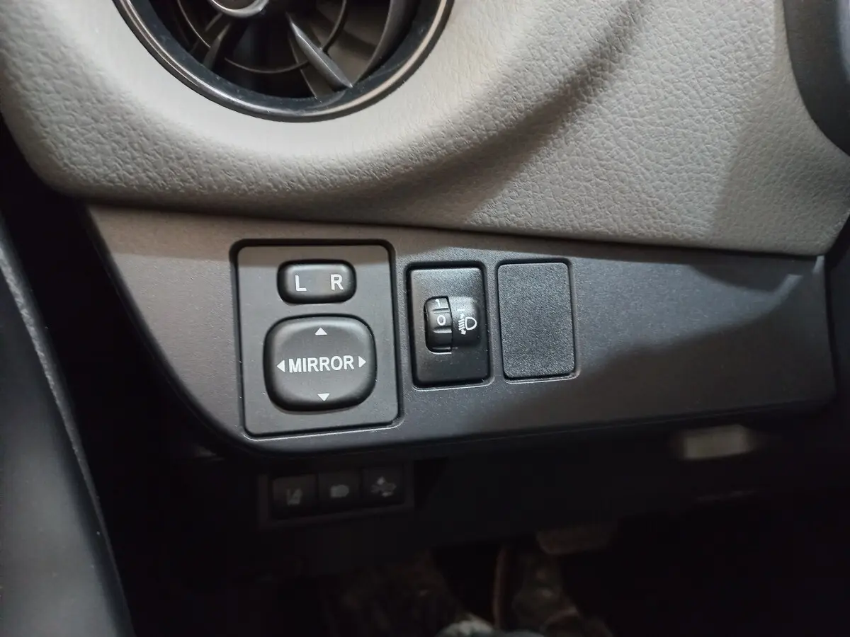 Vue rapprochée des commandes de réglage des rétroviseurs et des phares sur la Toyota Yaris blanche 2019.