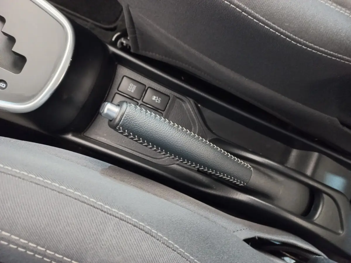 Vue rapprochée de la poignée de frein à main en cuir noir avec surpiqûres blanches dans l'habitacle de la Toyota Yaris hybride blanche.