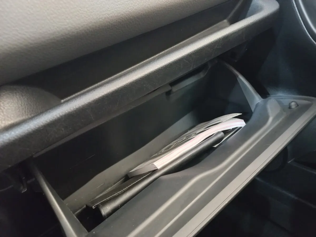 Gros plan sur la boîte à gants ouverte de la Toyota Yaris 1.5 VVT-I HYBRID France Business, intérieur noir.