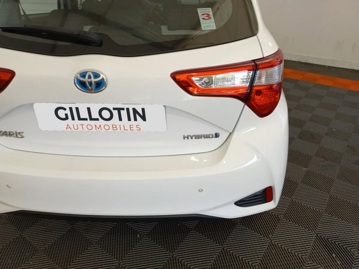 Vue arrière droite d'une Toyota Yaris blanche hybride avec feux arrière distinctifs et logo bleu Toyota.