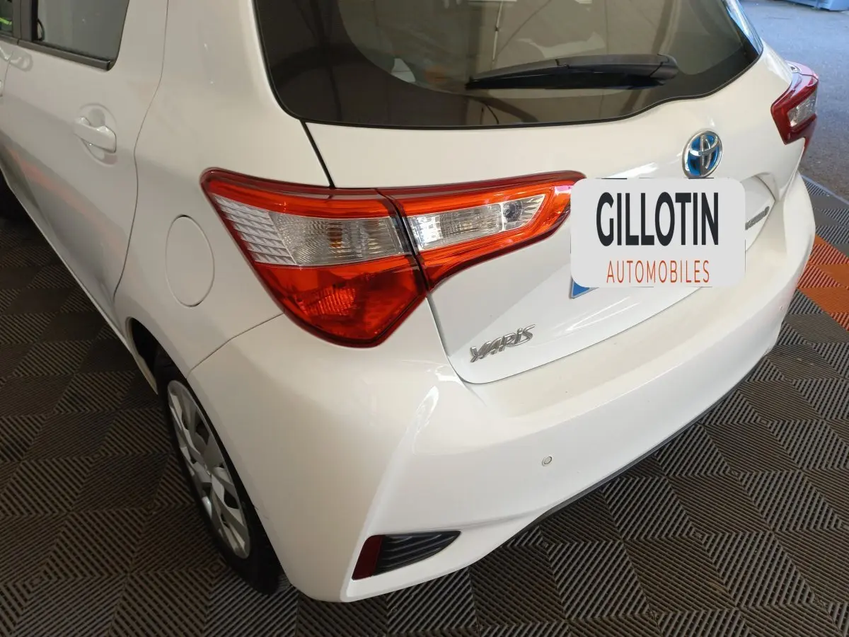 Vue 3/4 arrière gauche d'une Toyota Yaris blanche avec feux arrière distinctifs et badge modèle visible