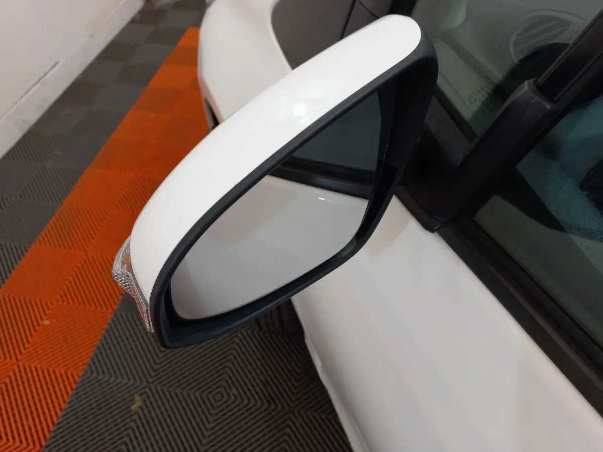 Rétroviseur côté gauche blanc de la Toyota Yaris hybride 2019, vue rapprochée sur fond de sol orange et gris.