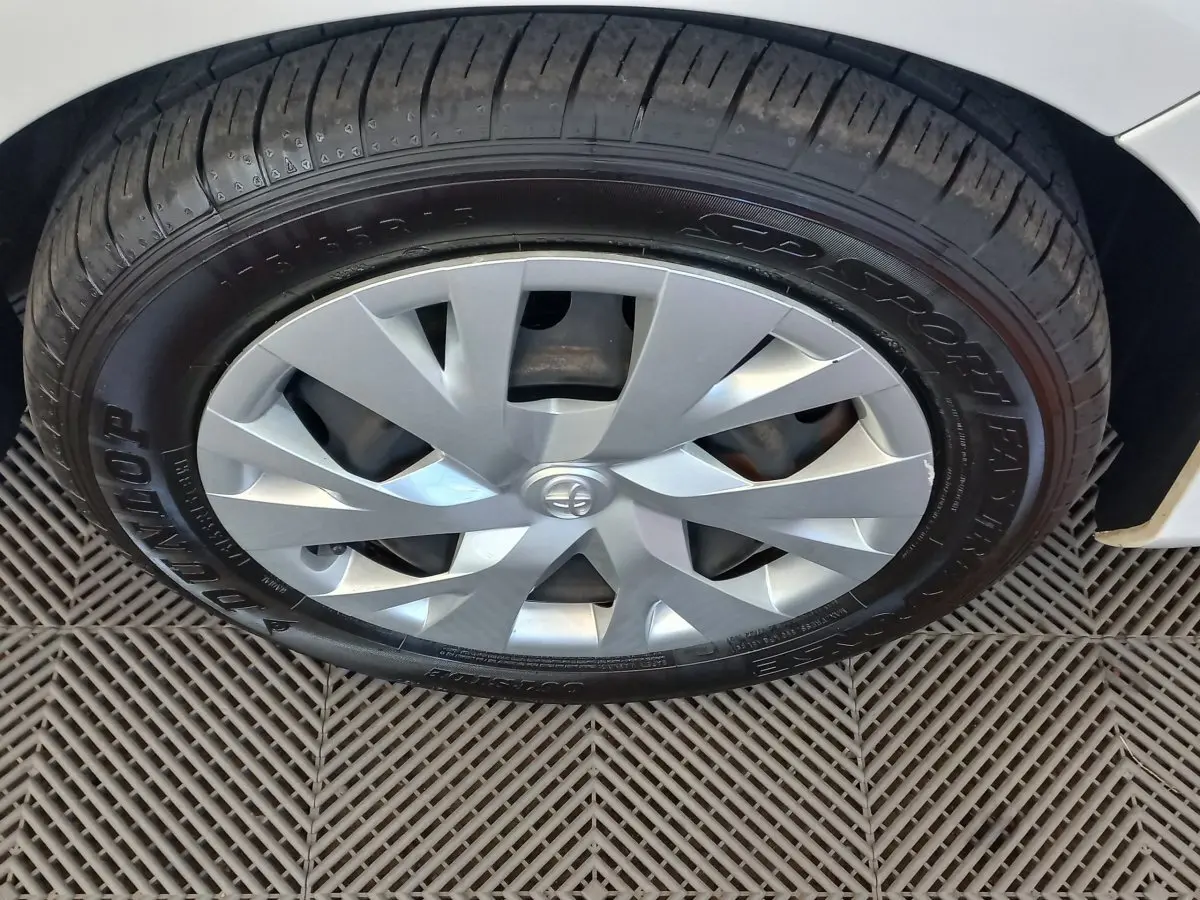Gros plan sur la roue avant gauche d'une Toyota Yaris blanche, avec enjoliveur argenté et pneu Dunlop.