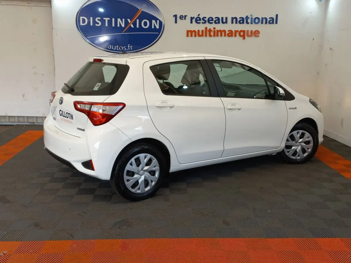 Toyota Yaris blanche vue de profil côté droit dans un showroom avec logo Distinxion en arrière-plan.