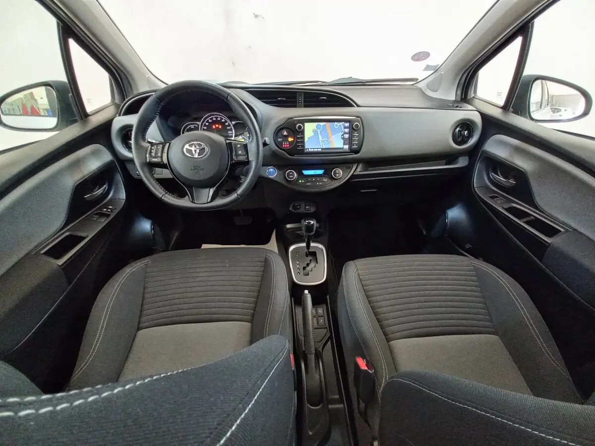 Vue intérieure avant de la Toyota Yaris 1.5 Hybrid 2019, tableau de bord noir avec écran tactile et sièges tissu gris.