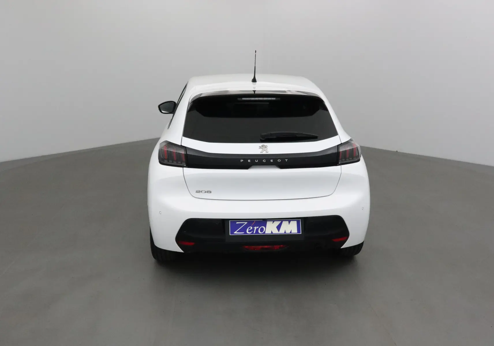 Vue arrière d'une Peugeot 208 blanche 2024 avec vitres teintées et logo Peugeot bien visible.