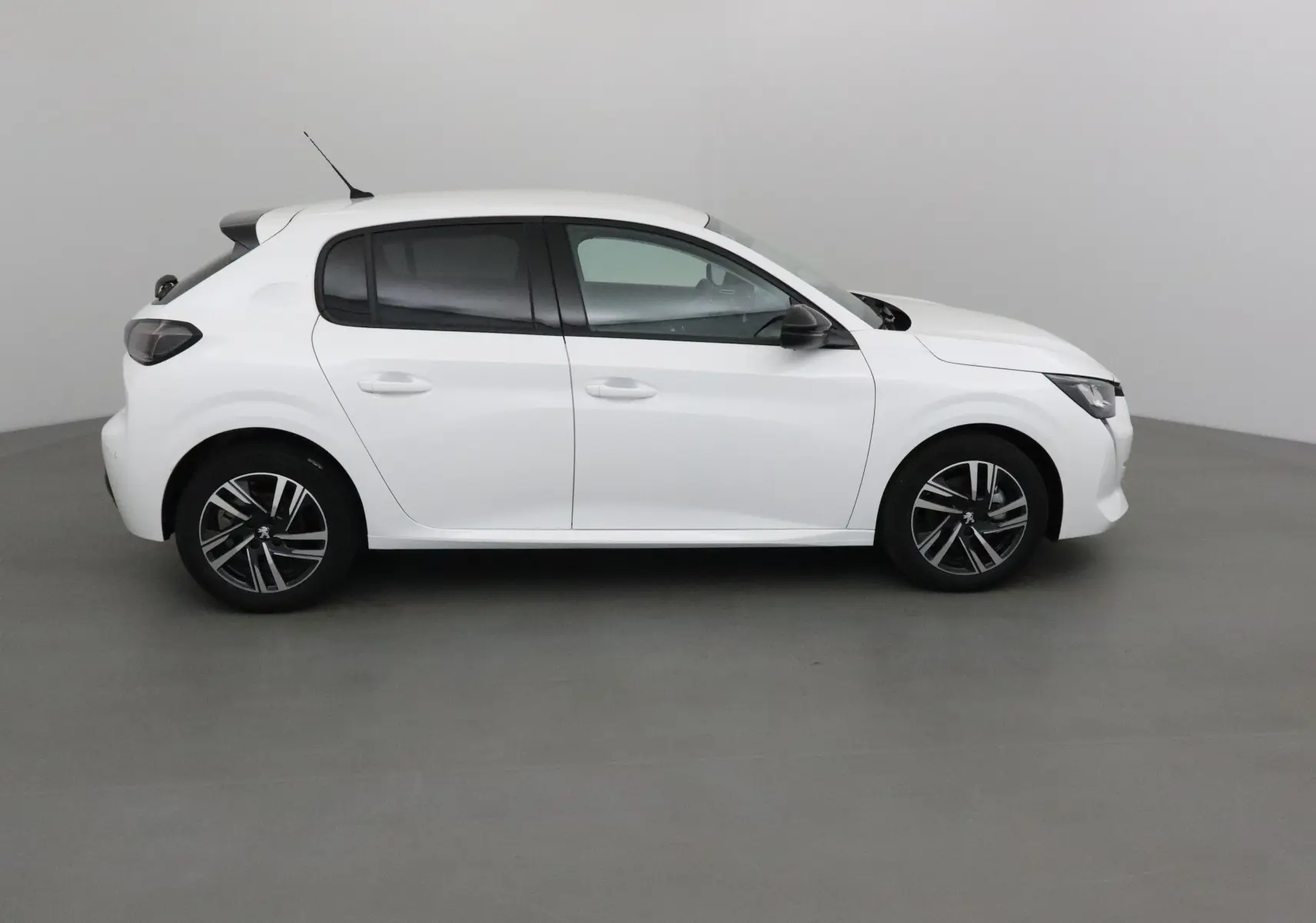 Profil côté droit d'une Peugeot 208 blanche 2024 avec jantes alliage noires et vitres teintées.