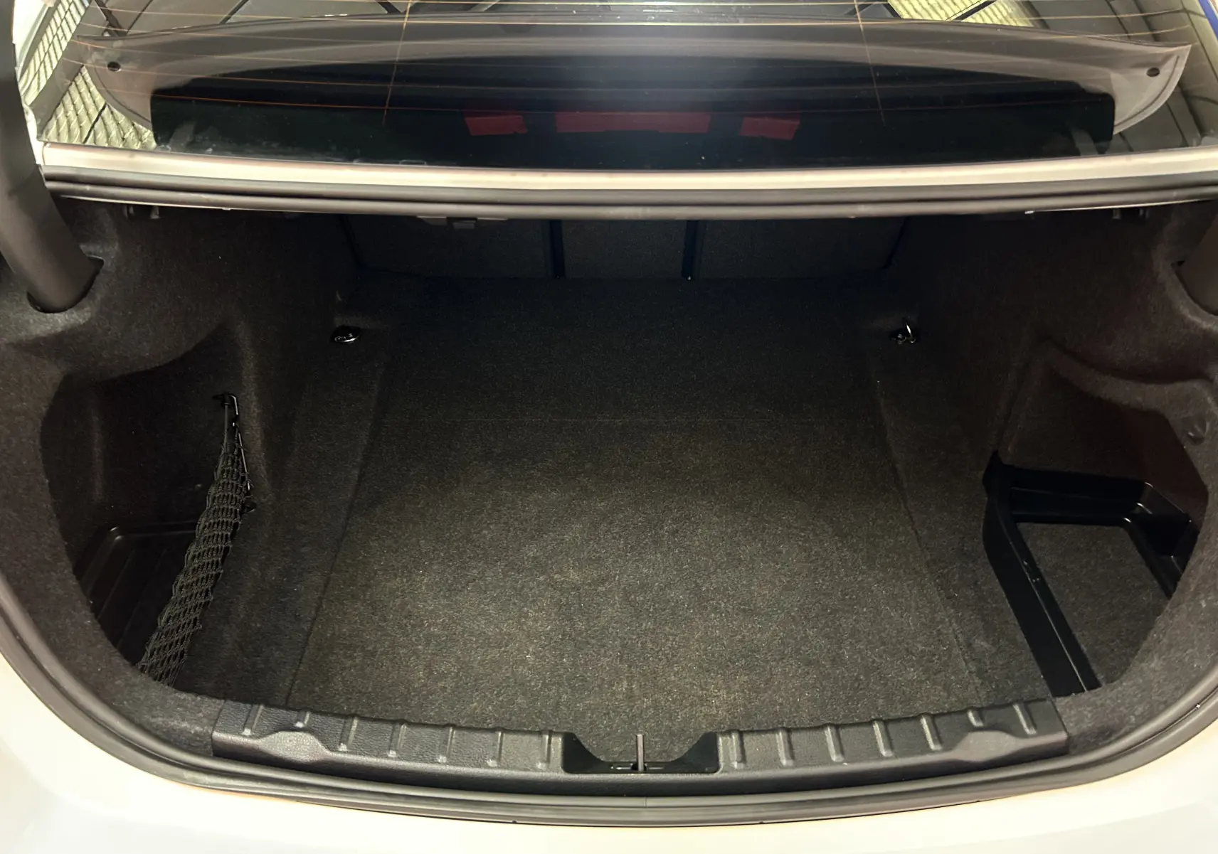 Coffre ouvert vu de l'arrière d'une BMW Série 3 320i blanche, montrant un espace de chargement propre et vide.