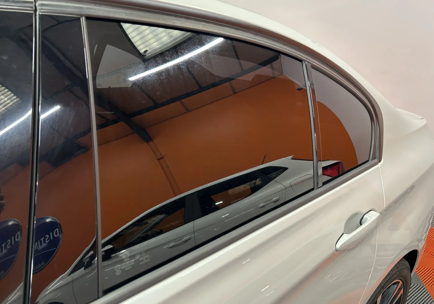 Vue latérale côté droit d'une BMW Série 3 blanche avec jantes sport et vitres teintées en intérieur showroom.