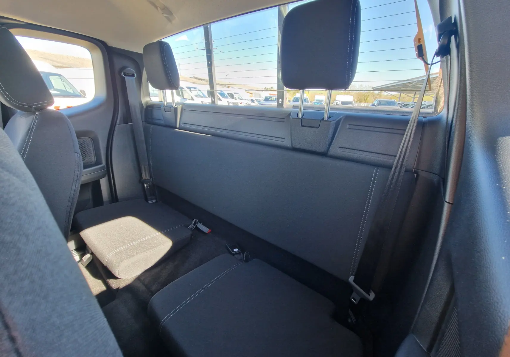 Vue intérieure arrière du Ford Ranger Super Cabine gris carbone, montrant les sièges arrière compacts et la vitre arrière.