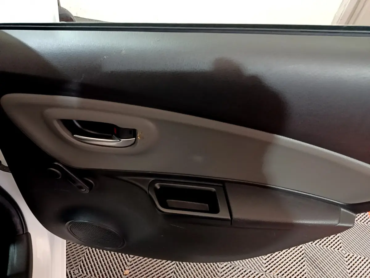 Vue rapprochée de la porte côté gauche de la Toyota Yaris blanche, montrant la poignée intérieure et le haut-parleur intégré.