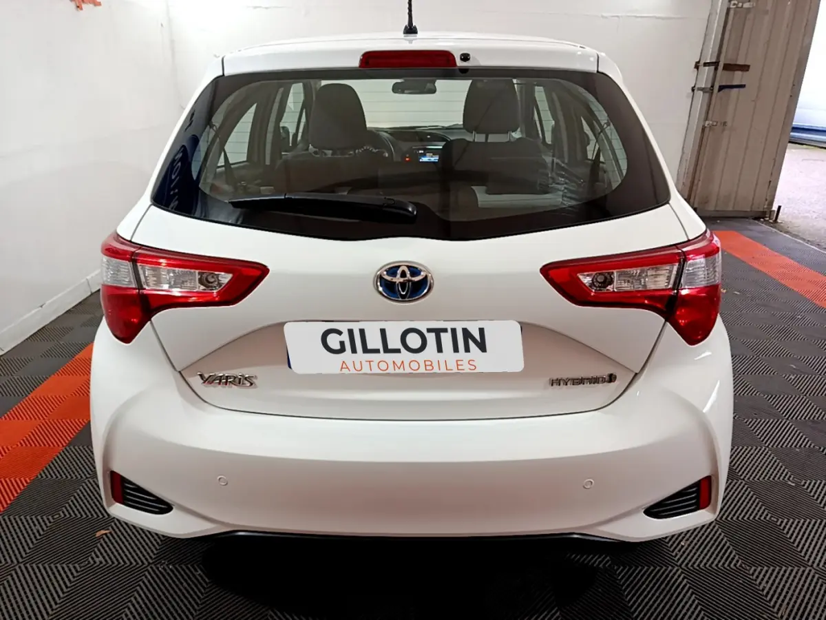 Vue arrière d'une Toyota Yaris blanche hybride 2020 avec feux arrière nets et logo Toyota visible.