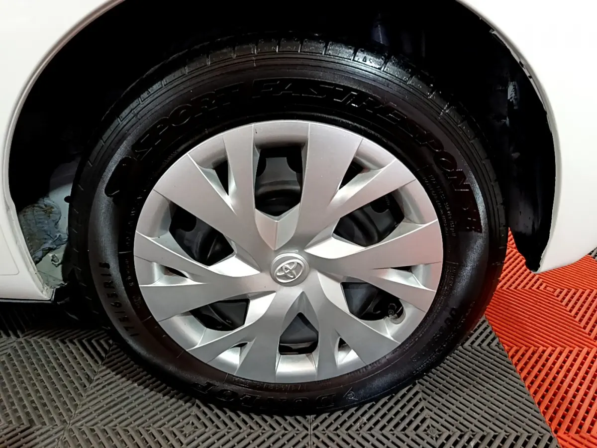 Gros plan sur la roue avant droite d'une Toyota Yaris blanche, avec enjoliveur argenté au design moderne.