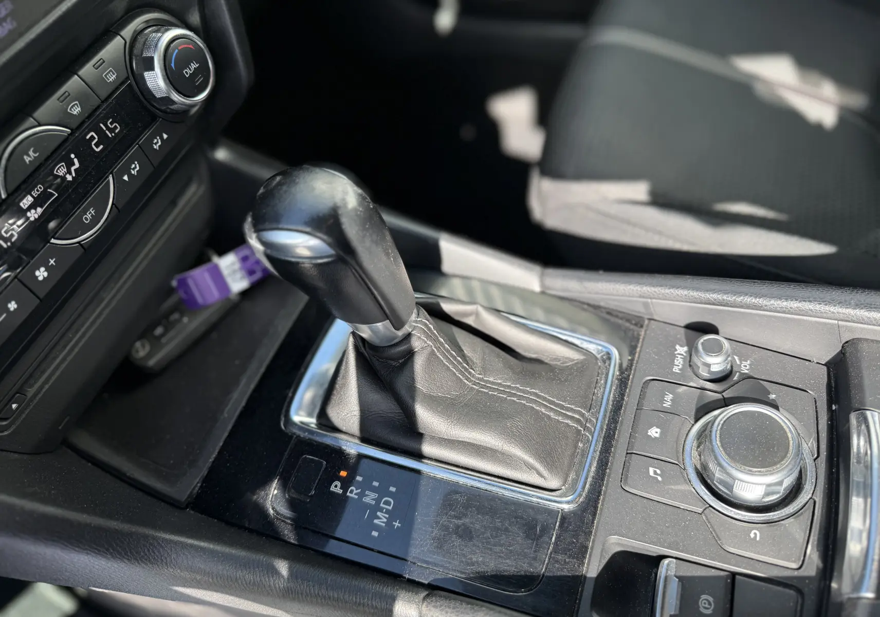 Gros plan sur la console centrale de la Mazda3 gris 2017, mettant en valeur le levier de vitesse automatique et les commandes multimédia.