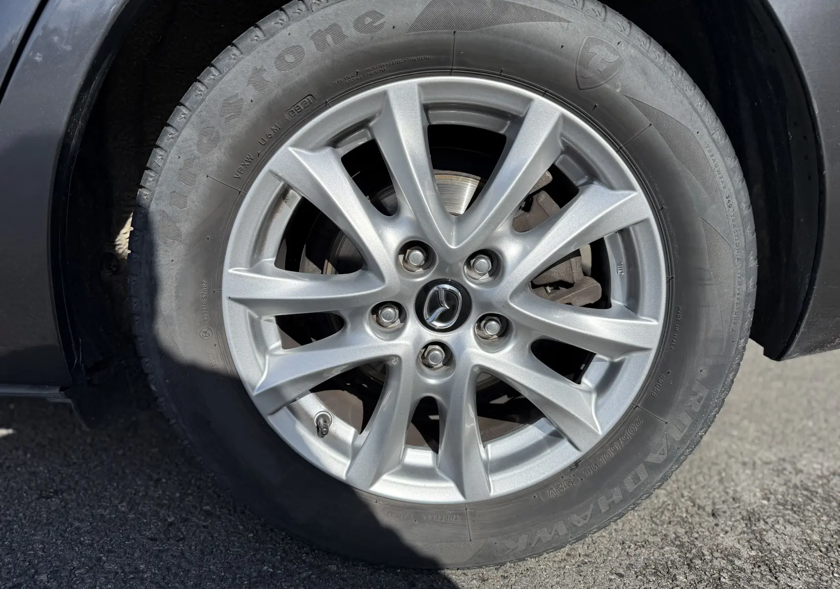 Gros plan sur la roue avant droite d'une Mazda3 gris 2017 avec jante alliage et pneu Firestone.