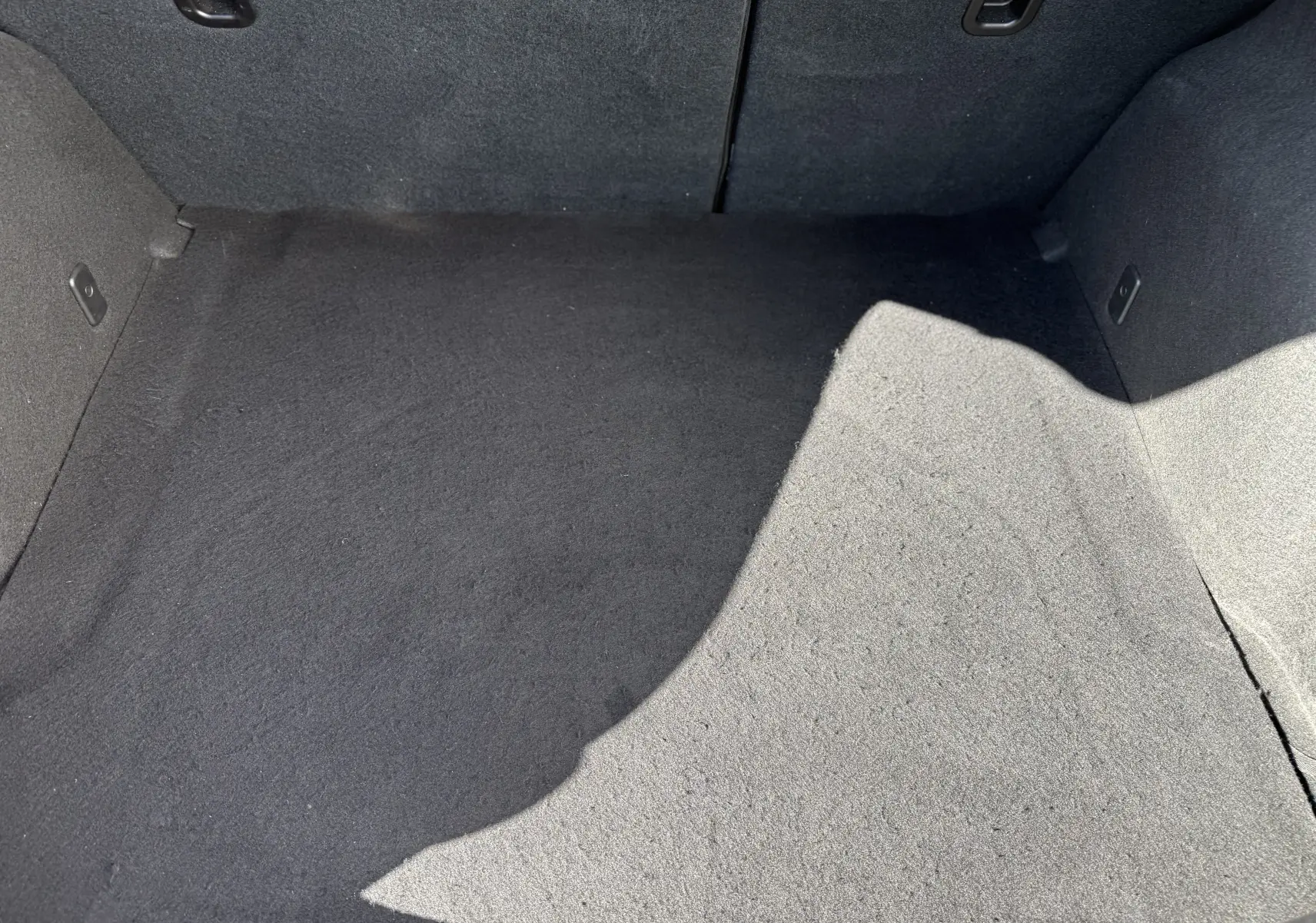 Vue rapprochée de l'intérieur du coffre gris foncé de la Mazda3 2017, montrant la moquette propre et les fixations latérales.