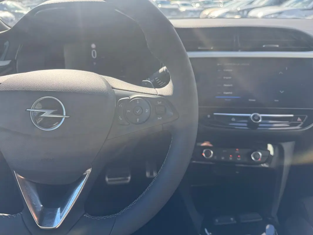 Vue intérieure centrée sur le volant Opel avec commandes intégrées et tableau de bord numérique flou en arrière-plan.