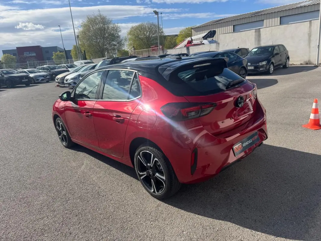 Vue 3/4 arrière droite d'une Opel Corsa rouge avec toit noir et jantes alliage 17 pouces, stationnée en extérieur.