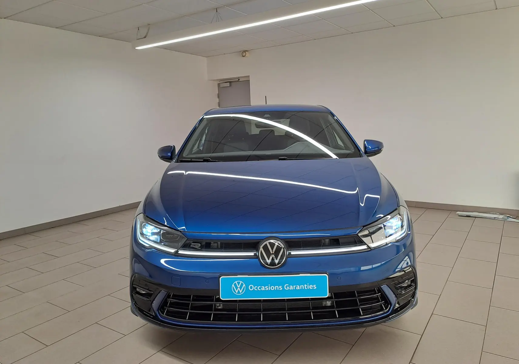 Vue de face d'une Volkswagen Polo 1.0 TSI R-Line bleu récif métallisé avec phares allumés en intérieur.