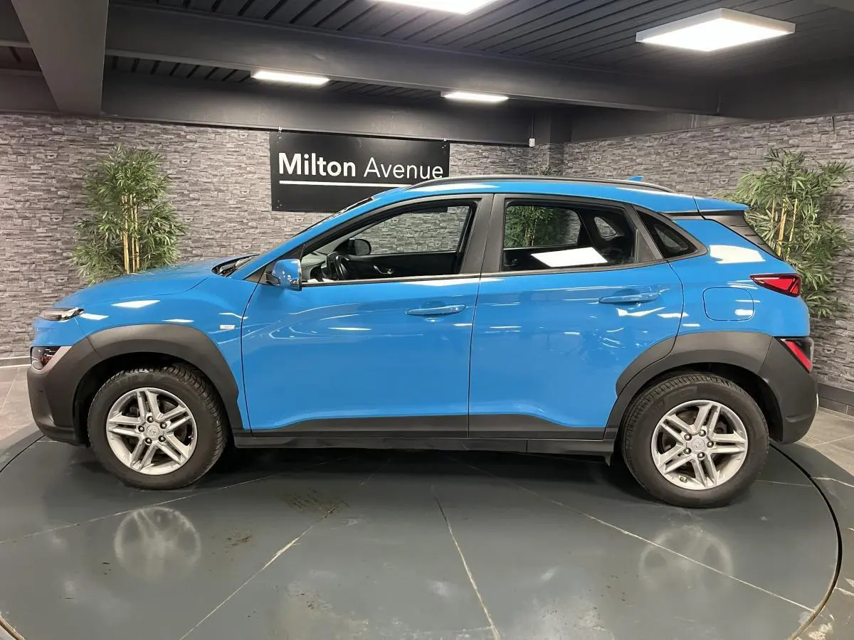 Vue de profil côté gauche d'un Hyundai Kona 1.6 CRDi Hybrid 48V bleu avec protections noires et jantes alliage 16 pouces.