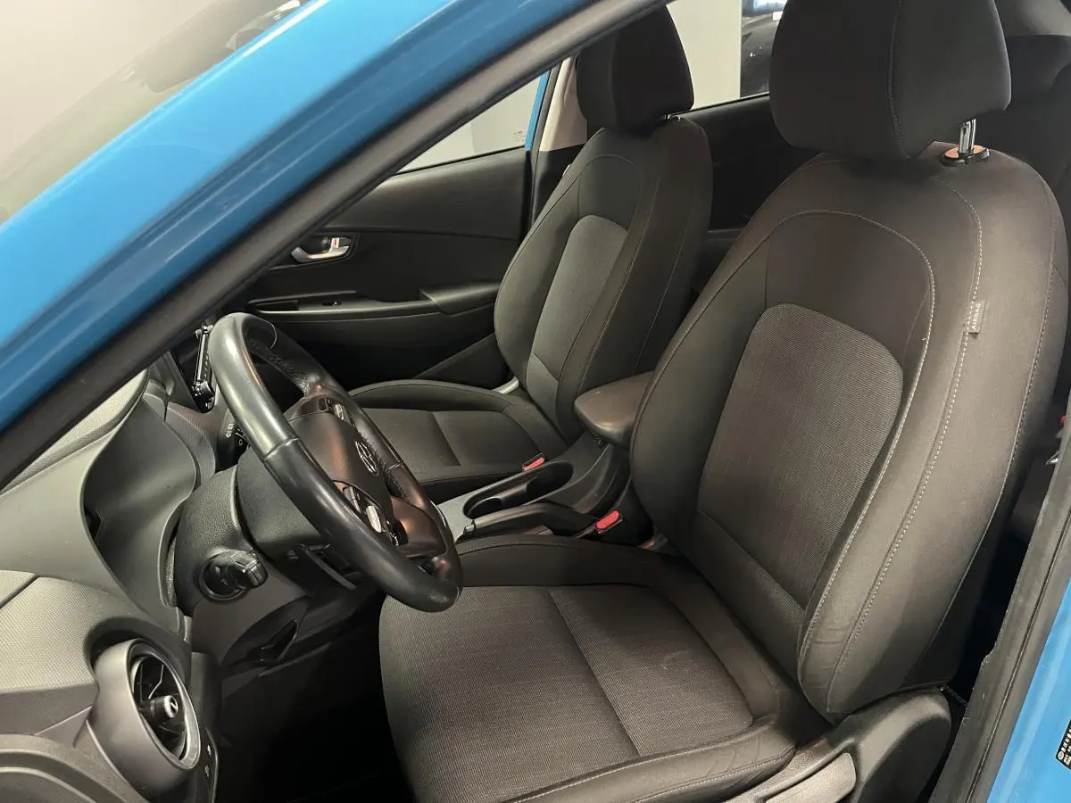 Vue intérieure côté conducteur du Hyundai Kona bleu 2022 montrant les sièges avant en tissu gris et le volant cuir.