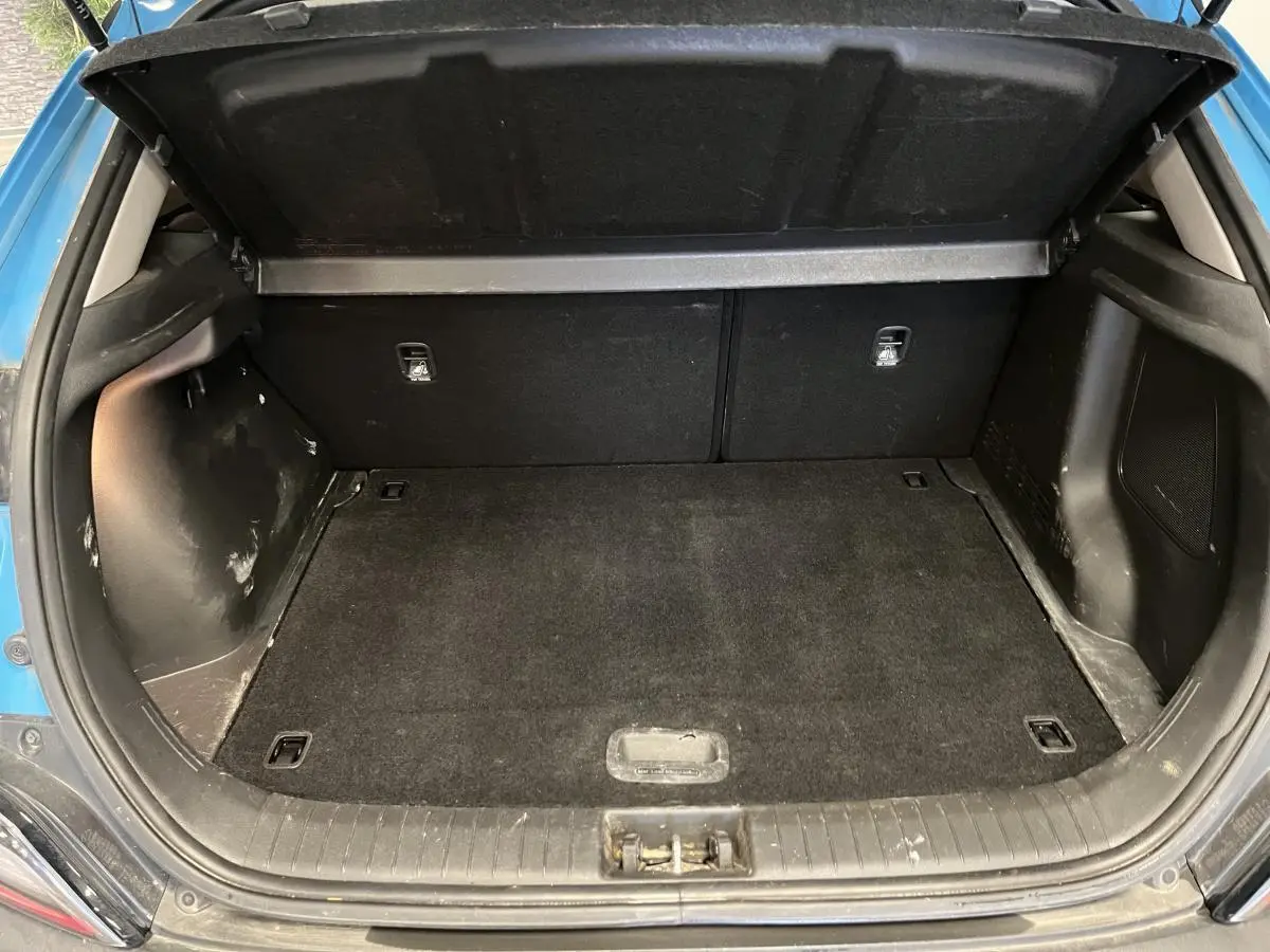 Coffre ouvert vu de l'arrière d'un Hyundai Kona bleu, montrant un espace de chargement propre et spacieux.