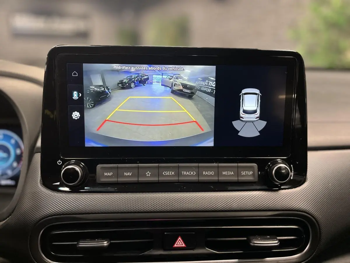 Écran tactile central affichant la caméra de recul et l’aide au stationnement du Hyundai Kona bleu 3/4 arrière.