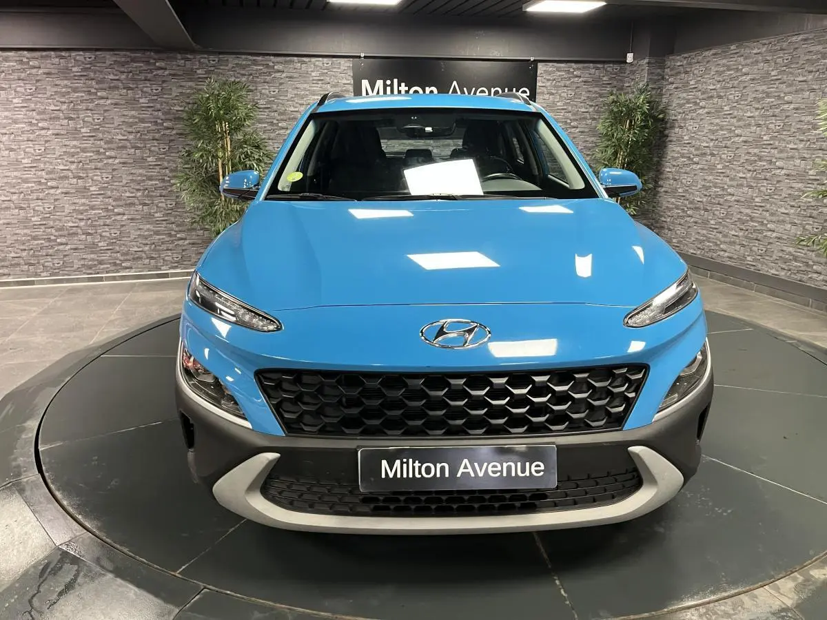 Vue avant d'un Hyundai Kona bleu avec calandre noire alvéolée et pare-chocs gris dans un showroom intérieur.