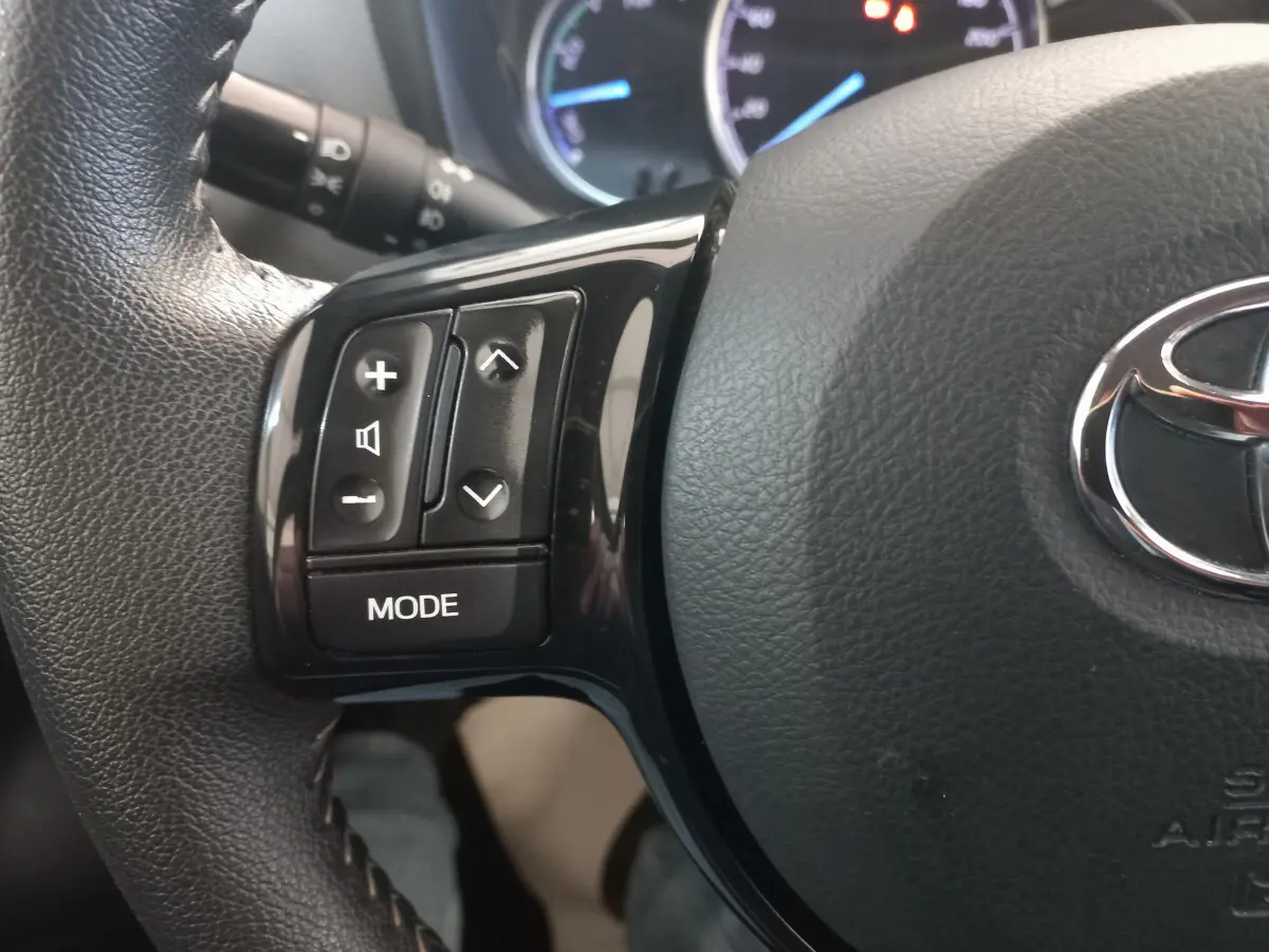 Gros plan sur les commandes gauche du volant cuir noir de la Toyota Yaris hybride 2018 avec logo Toyota visible.