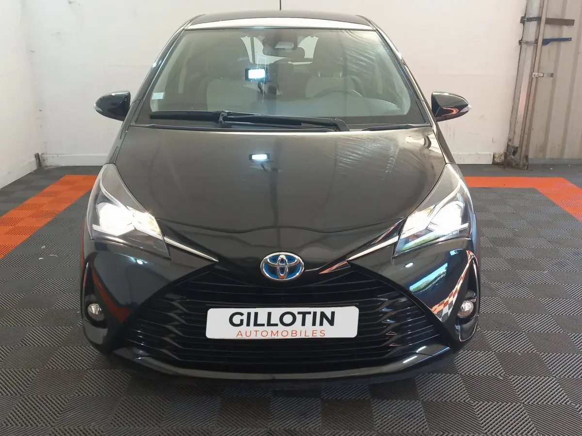 Vue frontale d'une Toyota Yaris noire 2018 avec phares allumés et calandre marquée en X.