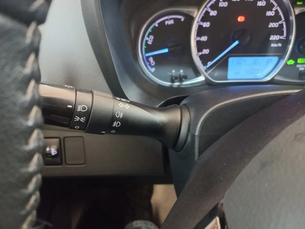 Gros plan sur le commodo gauche et le tableau de bord éclairé de la Toyota Yaris hybride noire, affichage digital bleu visible.