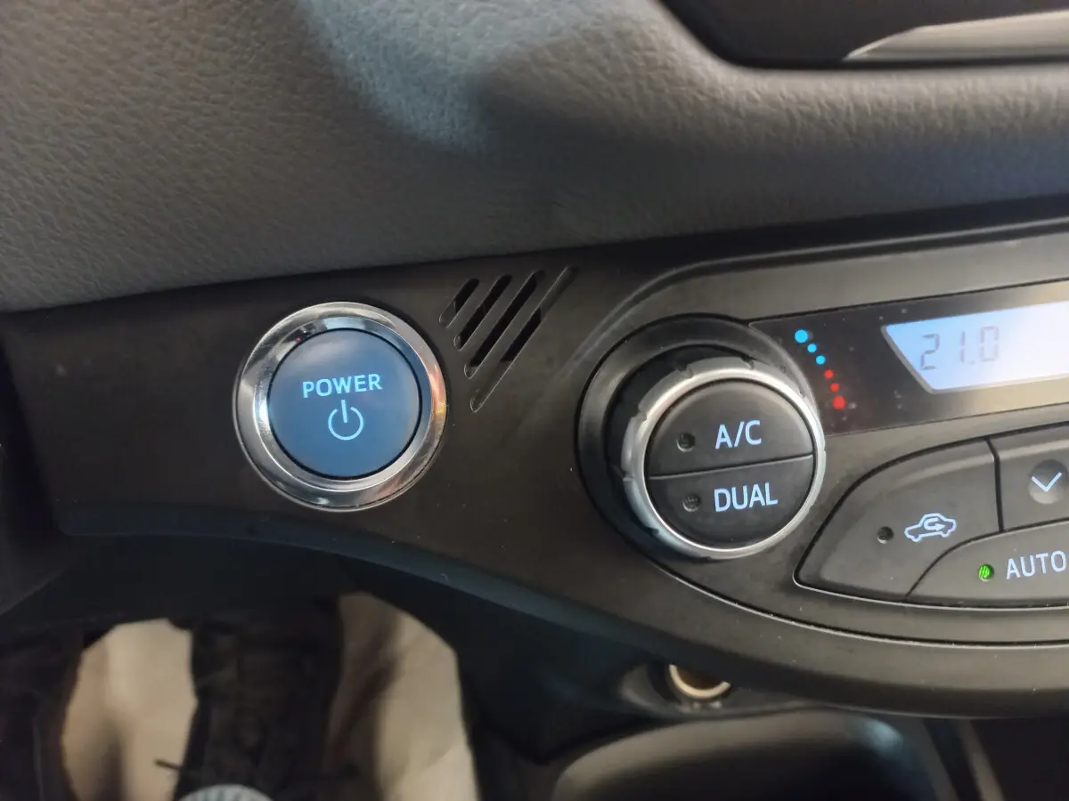 Détail du tableau de bord noir de la Toyota Yaris 2018 montrant le bouton Power bleu et la commande de climatisation dual zone.