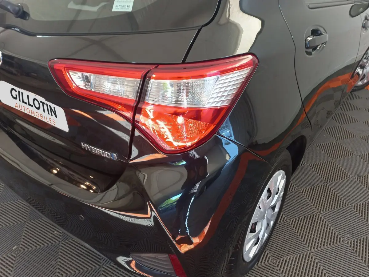 Vue 3/4 arrière droit d'une Toyota Yaris noire hybride avec feu arrière et badge Hybrid visibles.