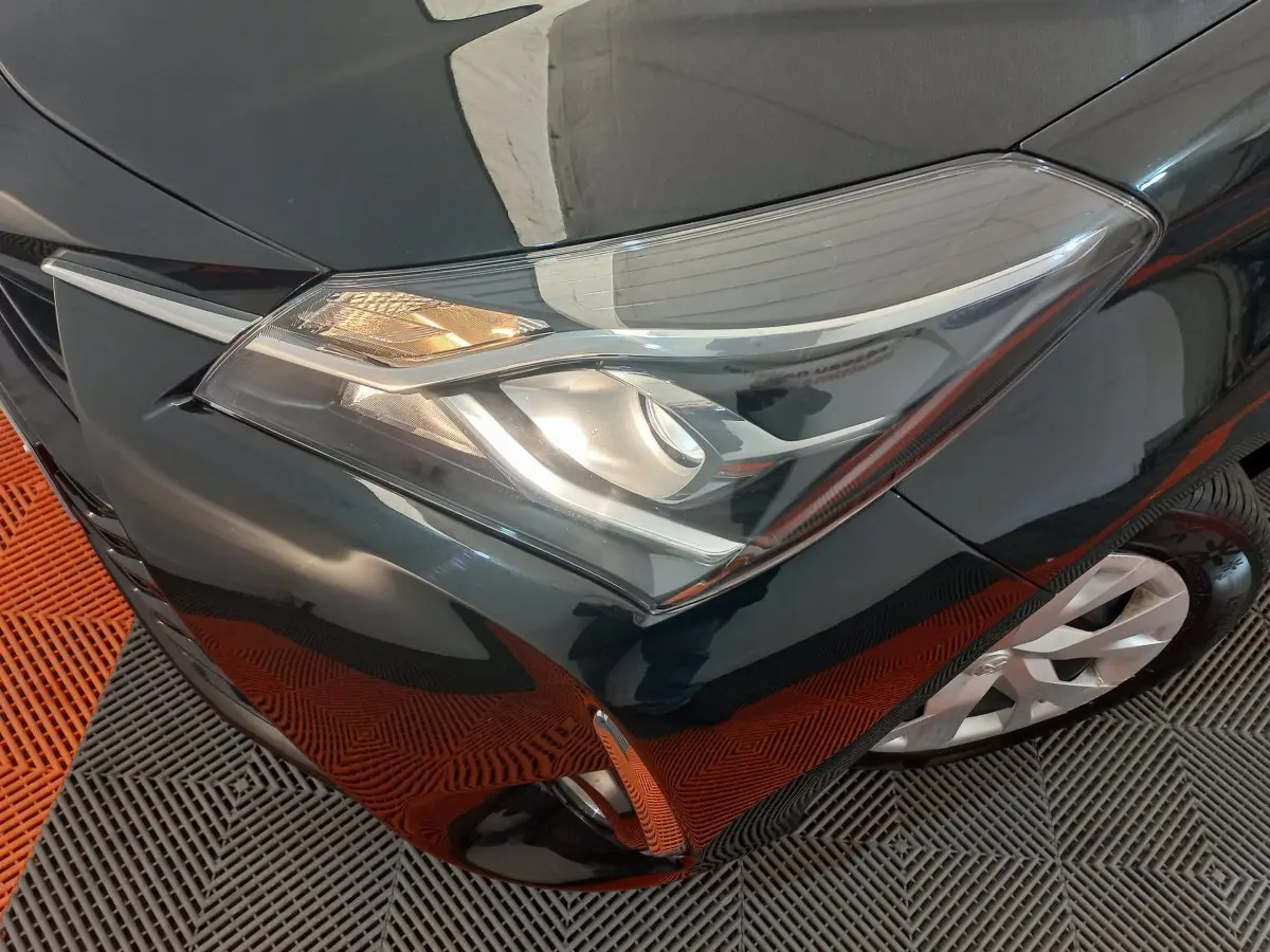 Gros plan sur le phare avant droit d'une Toyota Yaris noire, avec partie de la roue et pare-chocs visibles.
