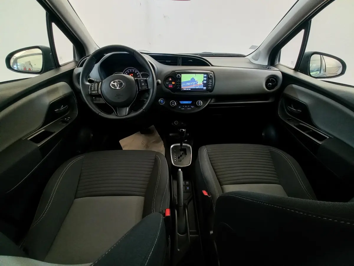 Vue intérieure avant de la Toyota Yaris noire 2018, tableau de bord avec écran tactile et volant multifonctions cuir.