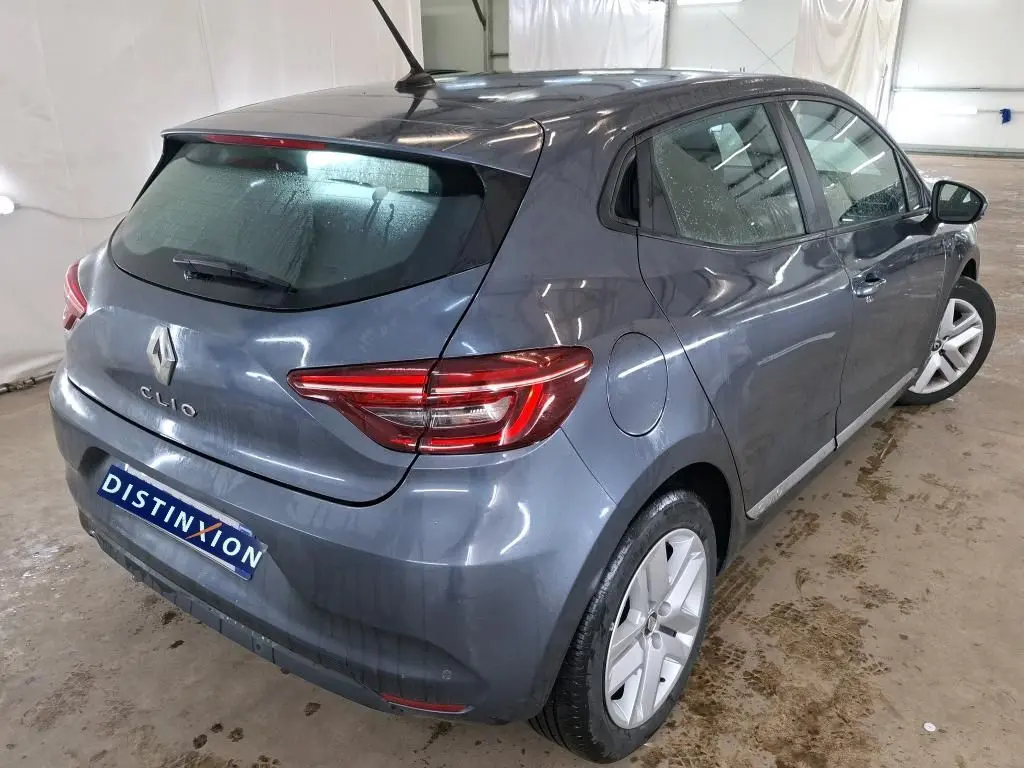 Vue 3/4 arrière droite d'une Renault Clio 5 portes Business gris titanium avec feux arrière allumés dans un garage.