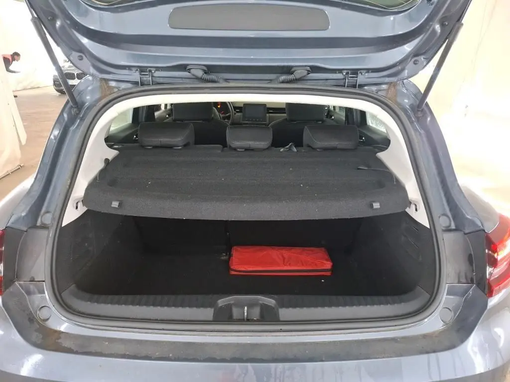 Coffre ouvert d'une Renault Clio 5P Business gris titanium, vue arrière montrant l'intérieur du coffre avec un objet rouge.