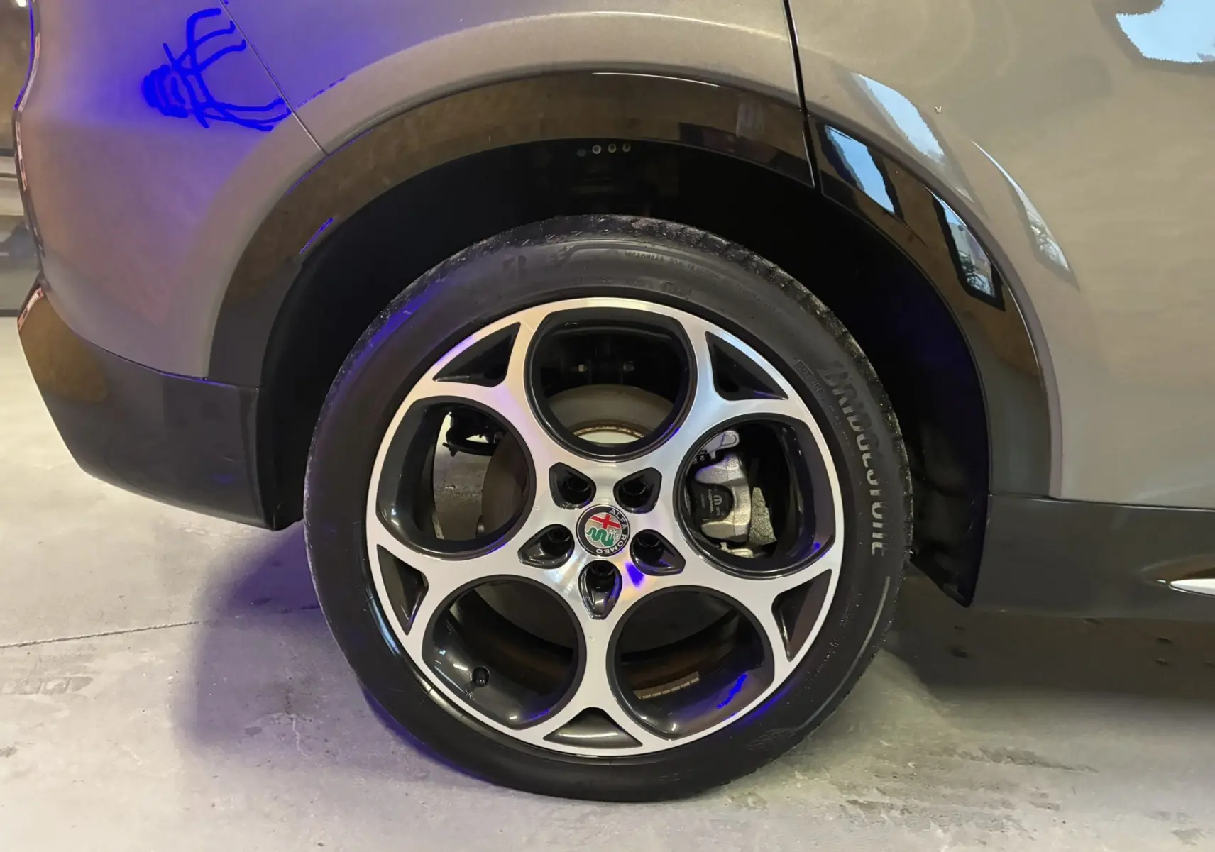 Gros plan sur la roue arrière droite d'une Alfa Romeo Tonale gris foncé avec jante alliage à cinq branches circulaires.