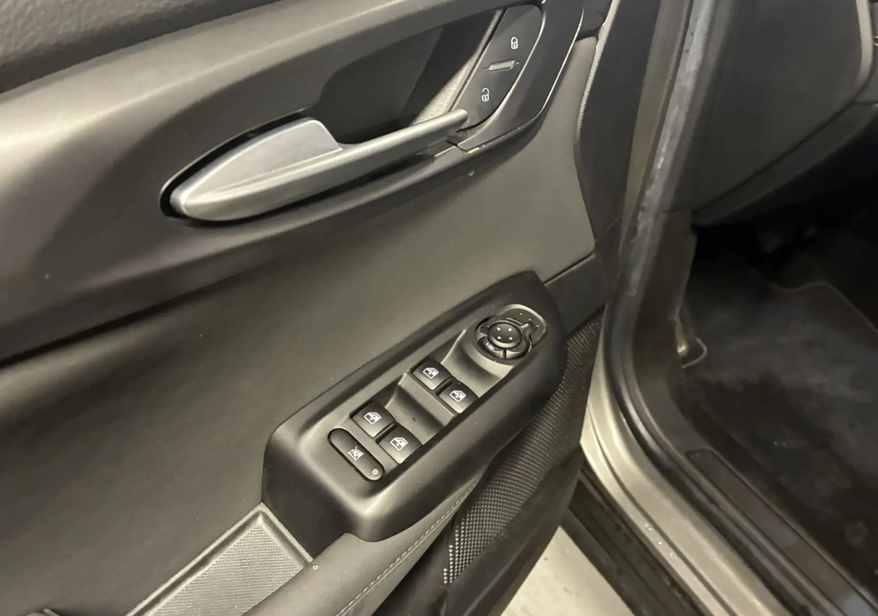 Gros plan sur la porte avant gauche de l'Alfa Romeo Tonale gris foncé, montrant les commandes des vitres et des rétroviseurs.