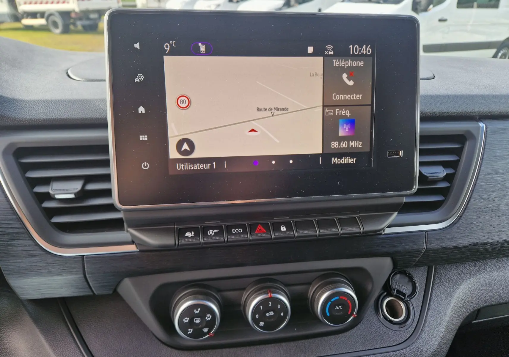 Vue rapprochée du tableau de bord du Nissan Primastar blanc 2025, mettant en valeur l’écran tactile et les commandes de climatisation.