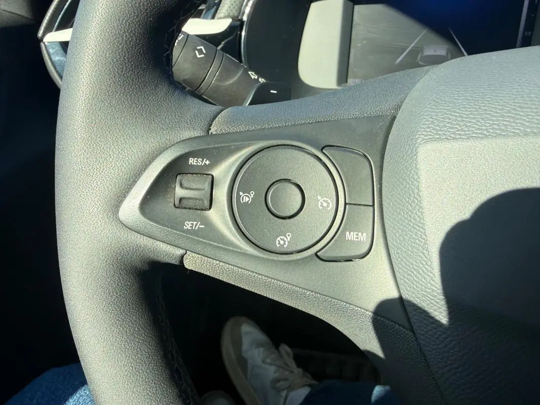 Gros plan sur les commandes de régulateur de vitesse au volant noir de l’Opel Corsa rouge 2025, version 1.2 Turbo Hybrid.