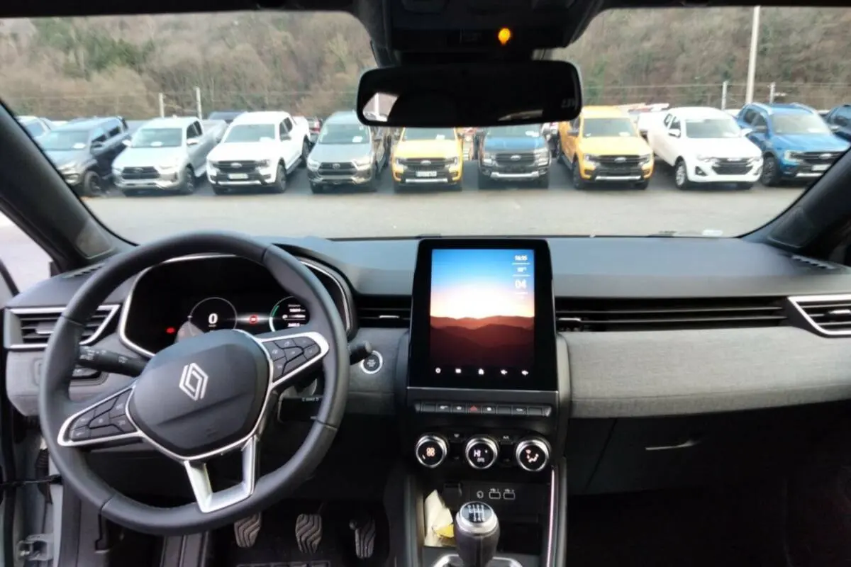 Vue intérieure avant de la Renault Clio gris rafale 2025, volant multifonctions et écran tactile vertical au centre.