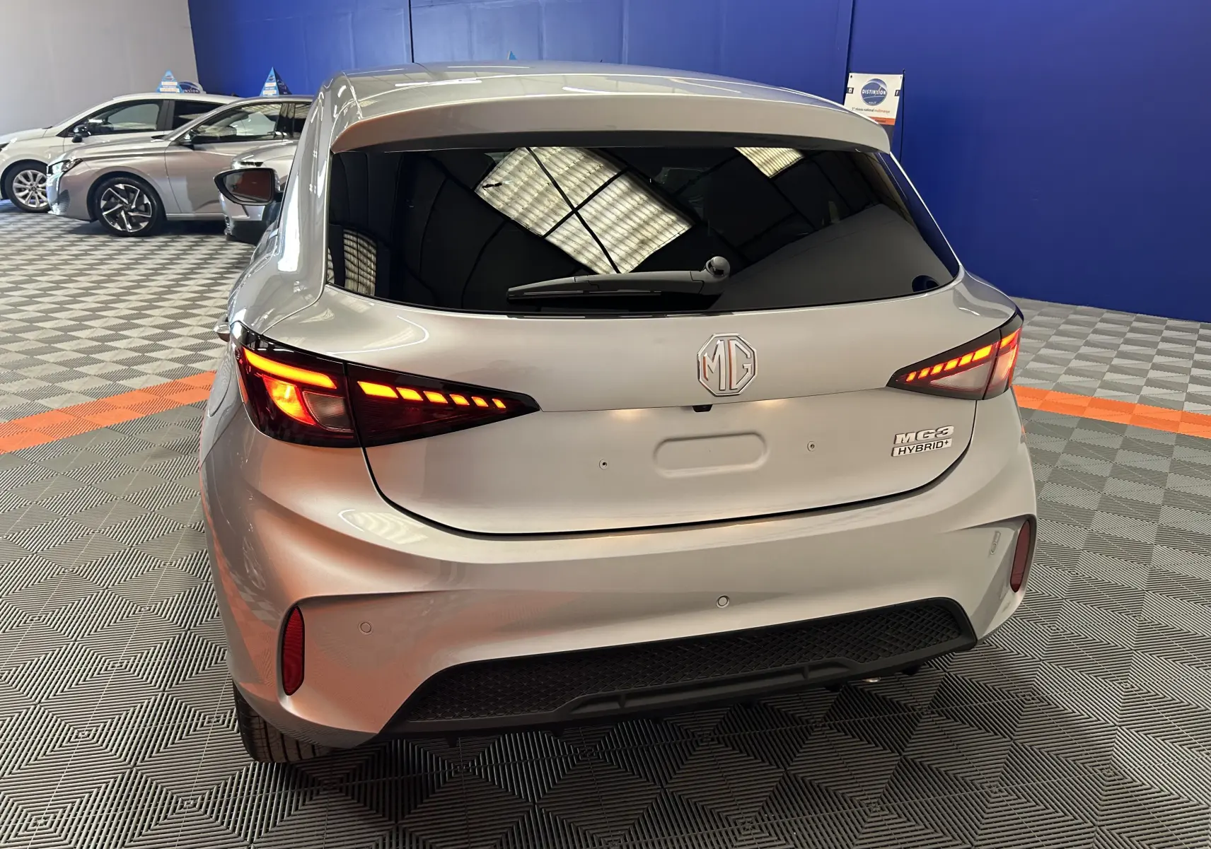 Vue arrière d'une MG3 Cosmic Silver 1.5 Hybrid+ 195 LUXURY avec feux LED allumés dans un showroom.