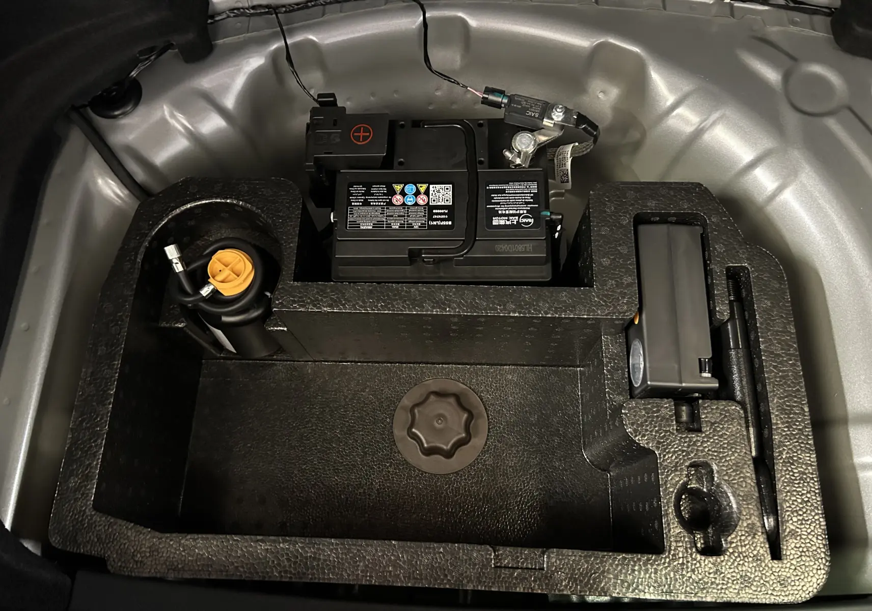 Vue plongeante sur le compartiment de rangement sous le coffre du MG3 Cosmic Silver, montrant la batterie et les outils.