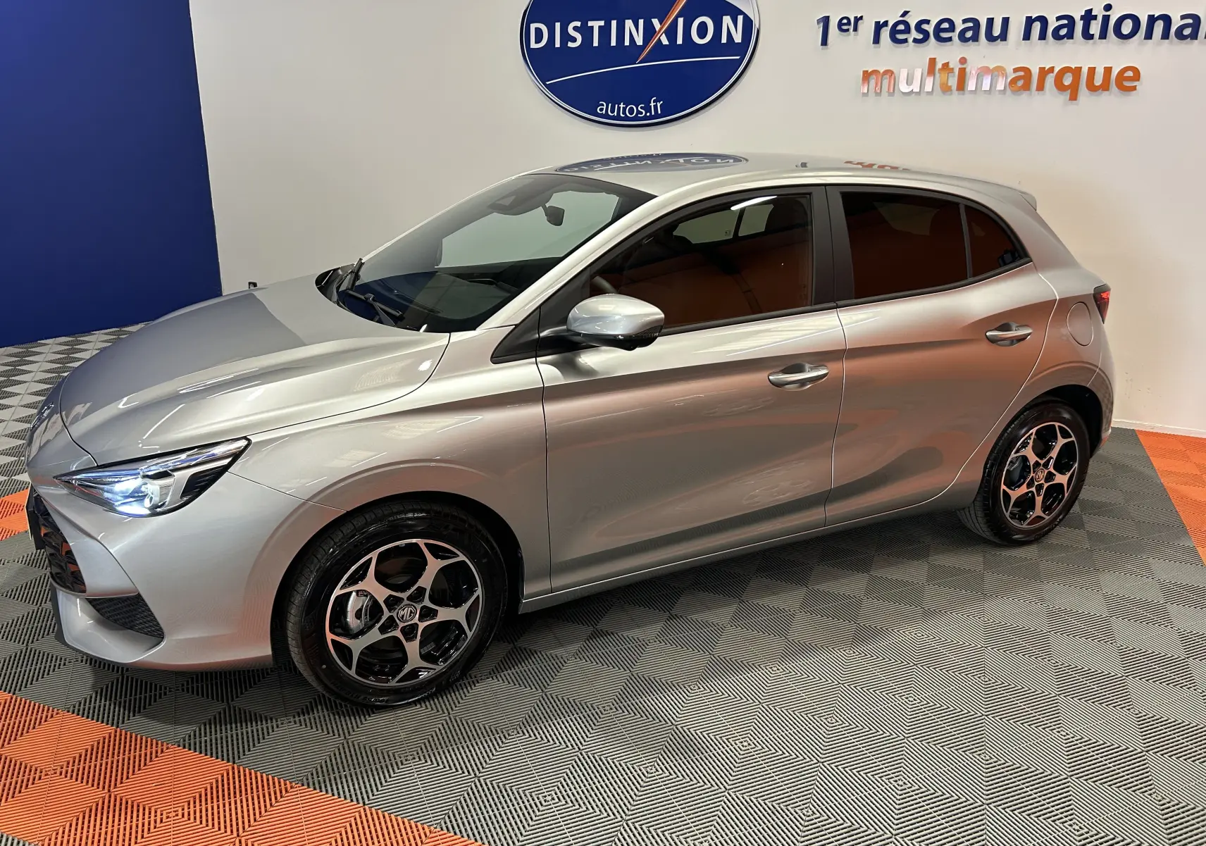Vue 3/4 avant droit de la MG3 Cosmic Silver 2026, hybride, avec jantes distinctives et phares LED allumés.
