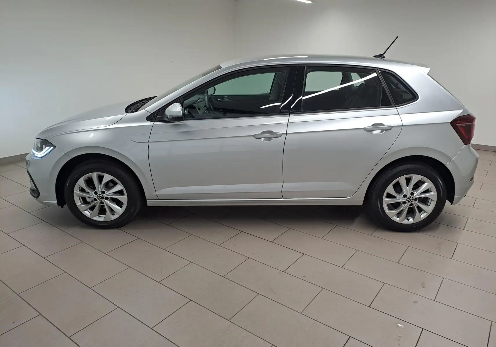 Profil droit d'une Volkswagen Polo 1.0 TSI 95 BVM5 Style 2025 en peinture reflet d'argent, avec feux avant allumés.