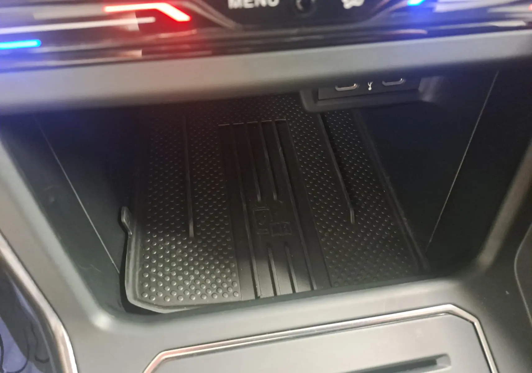 Gros plan sur la zone de rangement avant avec tapis antidérapant et éclairage LED rouge et bleu dans une Volkswagen Polo 2025.