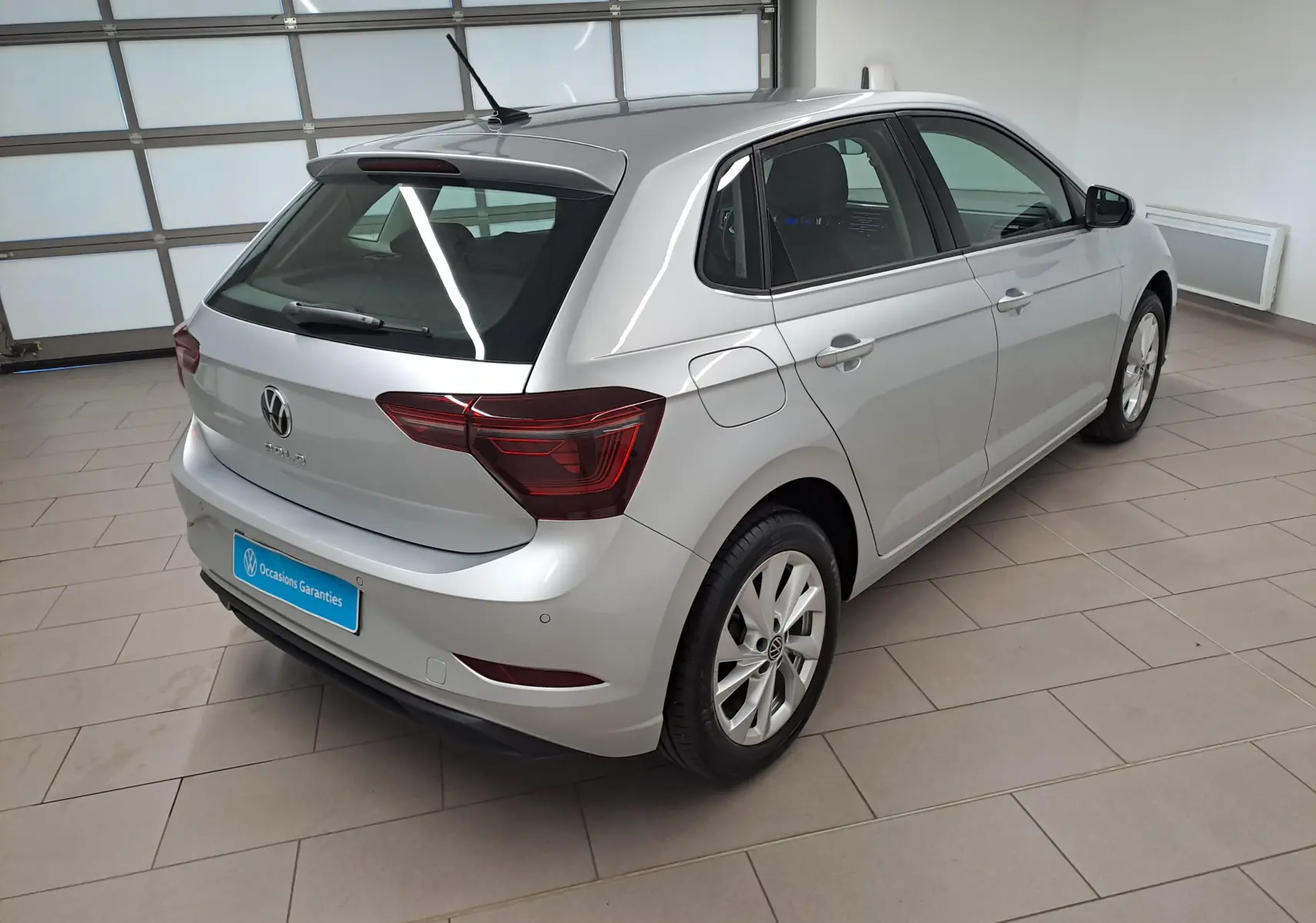 Vue 3/4 arrière droite d'une Volkswagen Polo 1.0 TSI Style argentée dans un showroom lumineux.