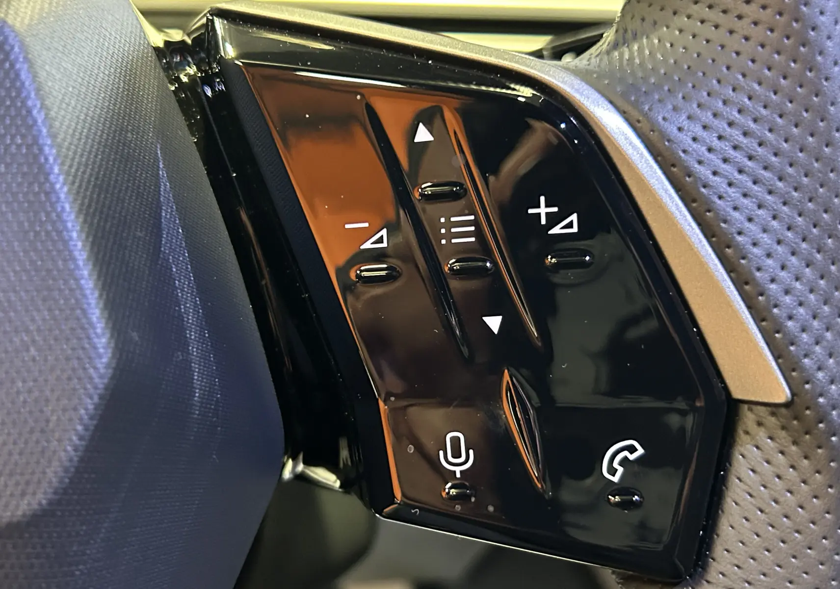 Gros plan sur les commandes noires brillantes du volant côté gauche du Peugeot 5008 Hybrid gris titane, boutons audio et téléphone.