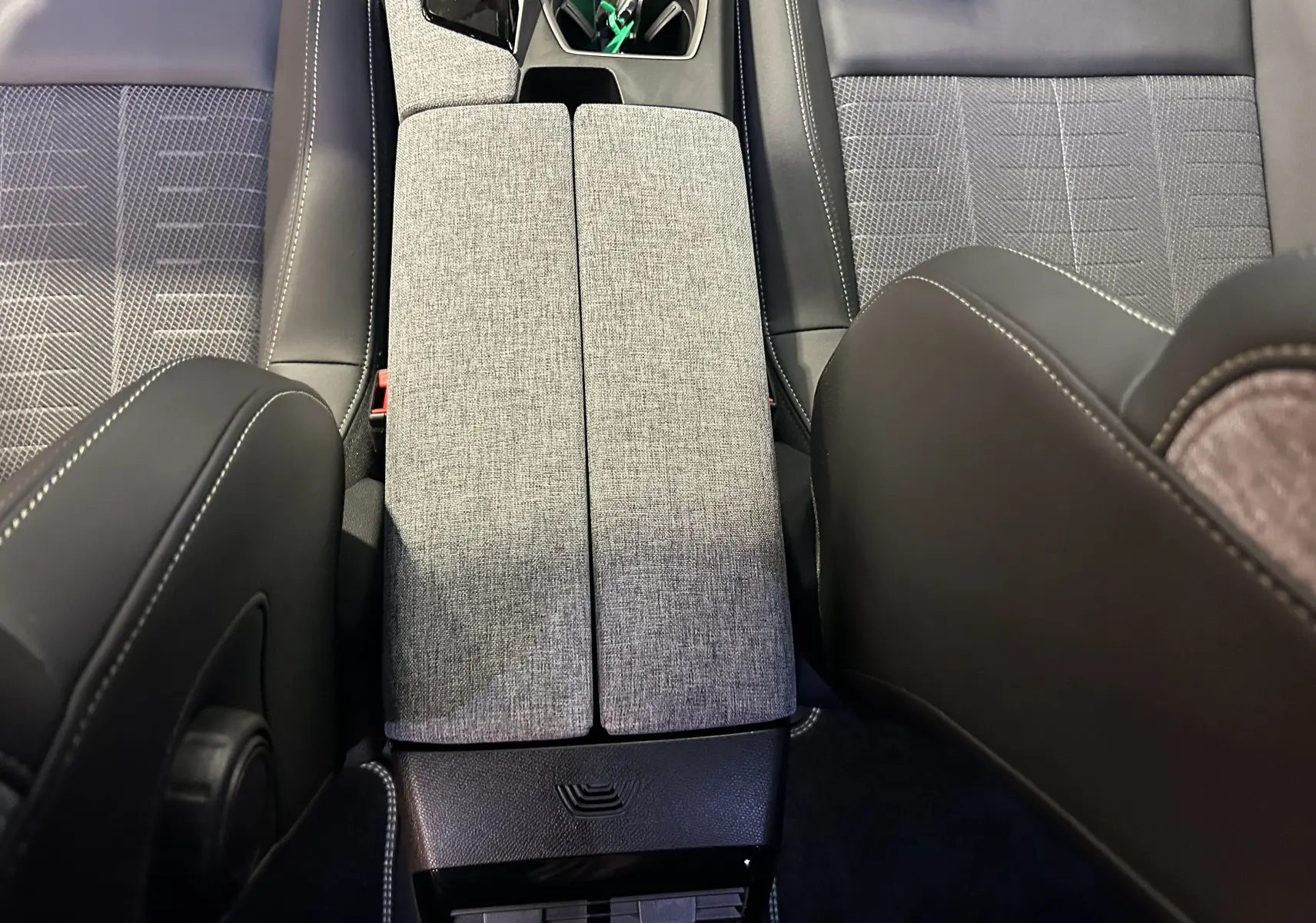 Vue intérieure centrée sur l'accoudoir central gris clair entre les sièges tissu et cuir du Peugeot 5008 Hybrid 2025.
